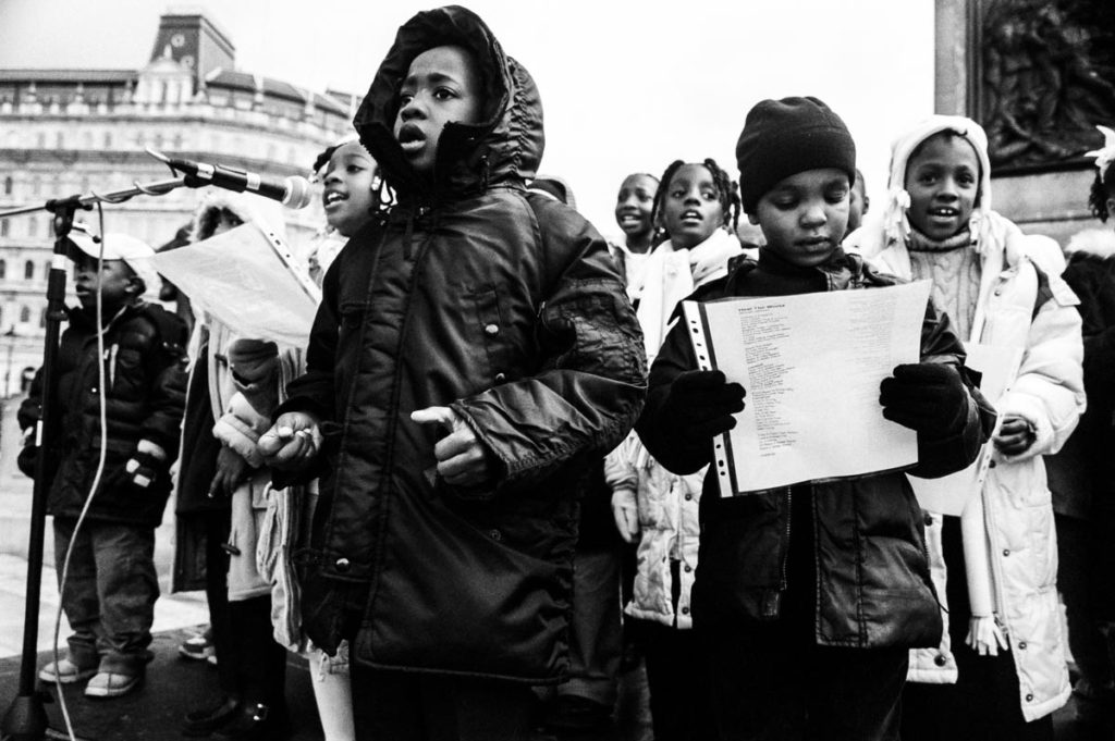 At the end of the 2004 Million Man March in London, against the backdrop of Nelson's Column in Trafalgar Square, children from the Nation of Islam sing “Heal the World” by Michael Jackson, London, England, 2004. Image copyright © Thaddeus Pope 2004.