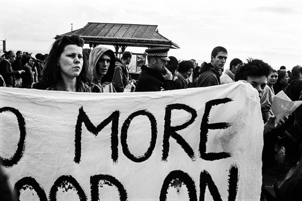 Anti-war protestors hold a banner that reads, ‘NO MORE BLOOD ON BRITISH HANDS’ on Brighton Seafront, England (2003). Image copyright © Thaddeus Pope