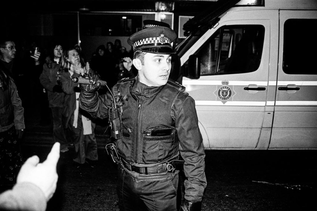 Armed with a baton, a British policeman uses force to control crowds of anti-war protestors in Brighton, England (2003). Image © Thaddeus Pope. (2/2)