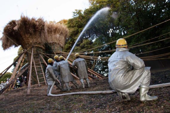 To avoid burning down the nearby forest, local firemen use a firehose to soak the trees surrounding the suzumi.
