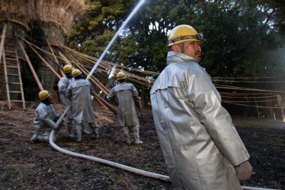 To avoid burning down the nearby forest, local firemen use a firehose to soak the trees surrounding the suzumi.