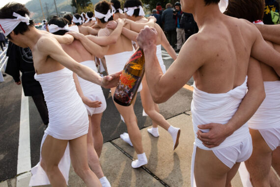 Sake bottles are passed between the men as they make their way towards the sea. The labels on the bottles show a graphic representation of the Toba Fire Festival.